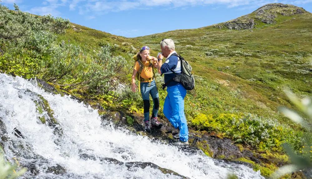 Grandfather and children take a break to drink mountain water from the stream during a mountain hike