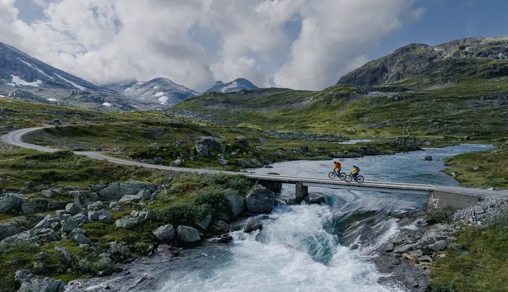 Young couple on a bike ride in Koldedalen cycling over a bridge with a magnificent backyard