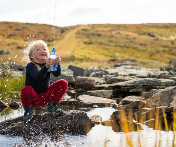 Jente leker med vann i en bekk på tur på Kongevegen over Filefjell