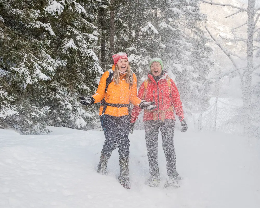 Two women on snowshoes smiling and laughing and throwing snow in the air