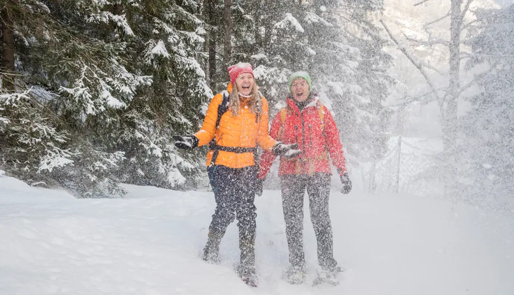 To kvinder på snesko smiler og griner og kaster sne op i luften