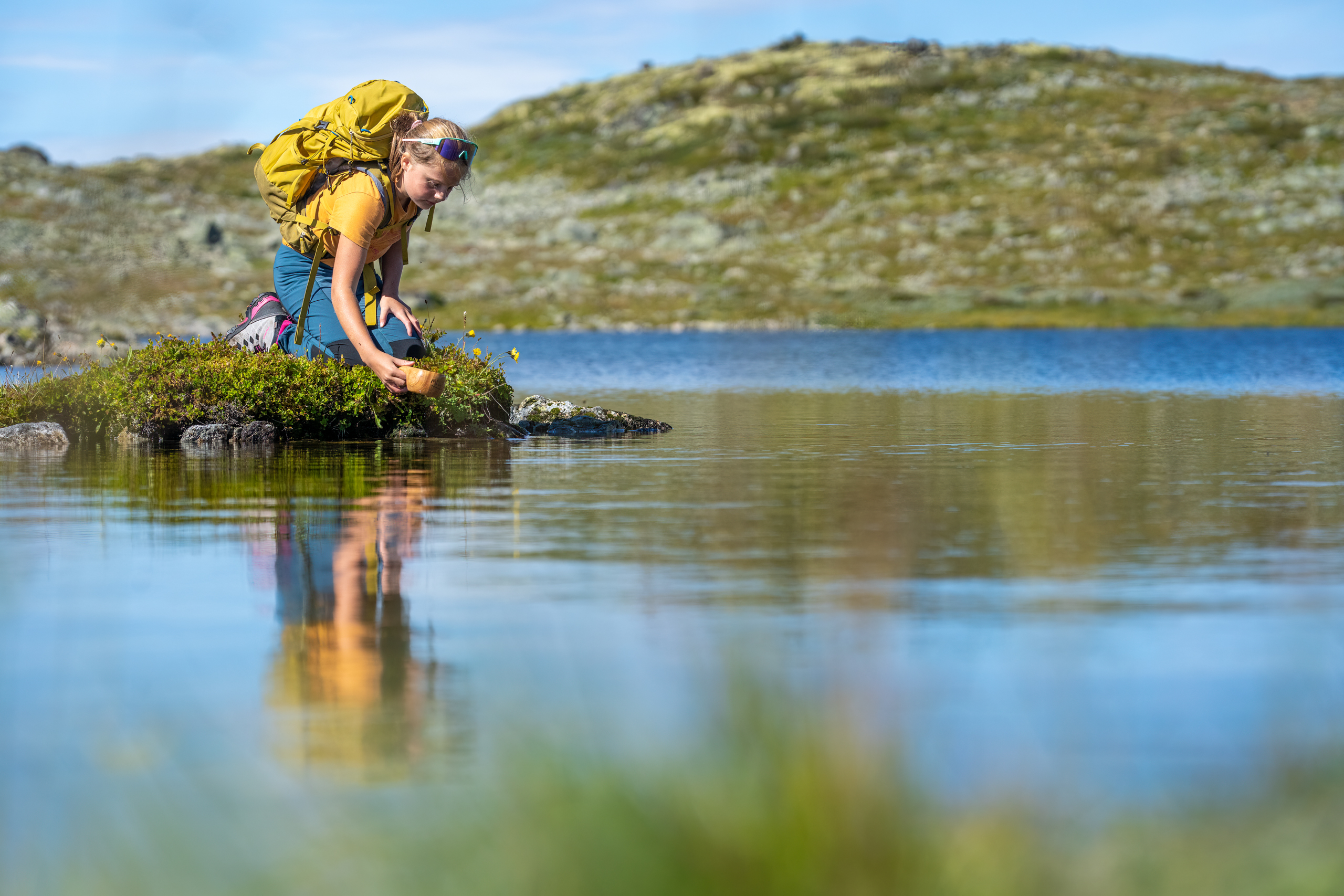 Young girl fills her cup with clean mountain water during a mountain hike