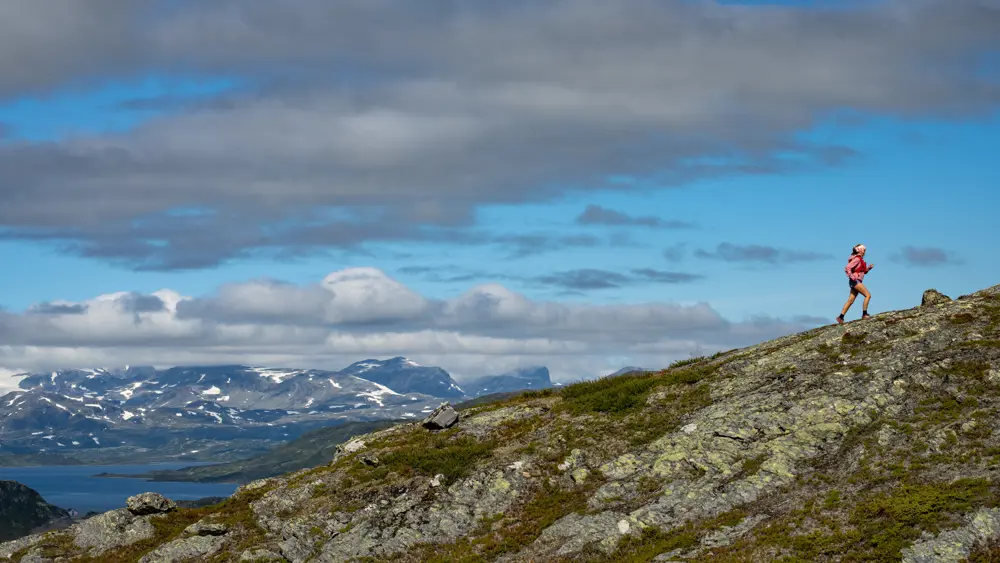 Trailløber i højfjeldet – ung kvinde løber med de majestætiske bjerge i Jotunheimen i baggrunden