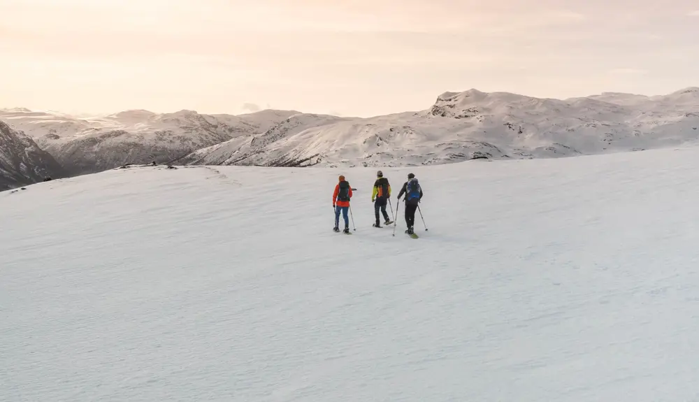 Tre personer på snesko i smuk aftensol ved Tyin Filefjell