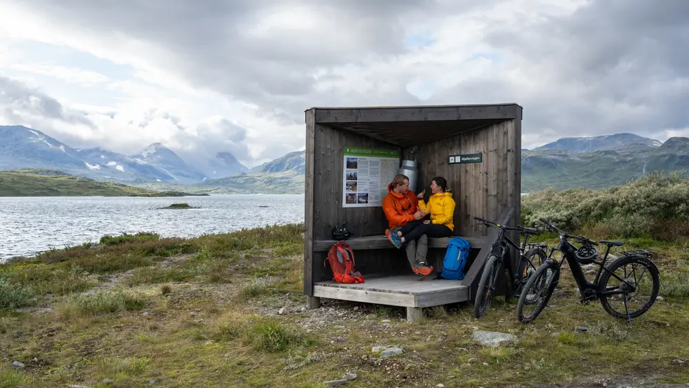 Ungt par på sykkeltur på Mjølkevegen langs Tyin tar matpause ved et informasjonspunkt