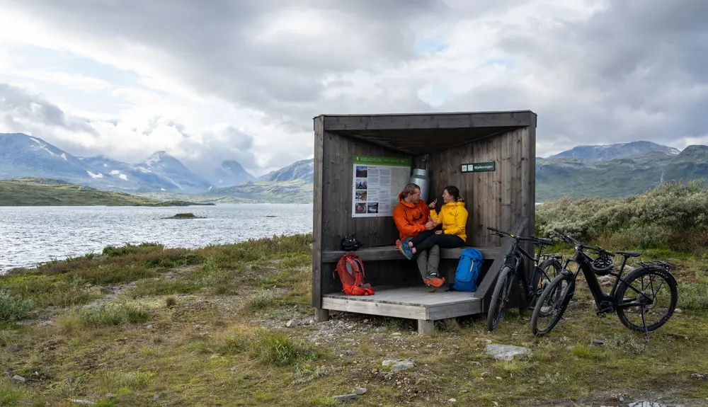 Young couple on a bike trip on Mjølkevegen along Tyin taking a food break at an information point