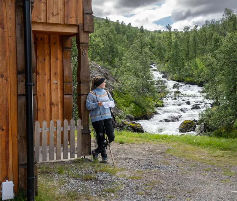 Young woman with fishing equipment looking at the river next to one of the apartments at Filefjellstuene