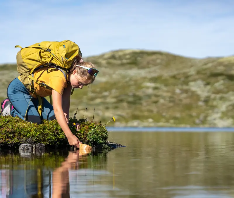 Ung pige fylder kop med rent bjergvand under bjergvandring