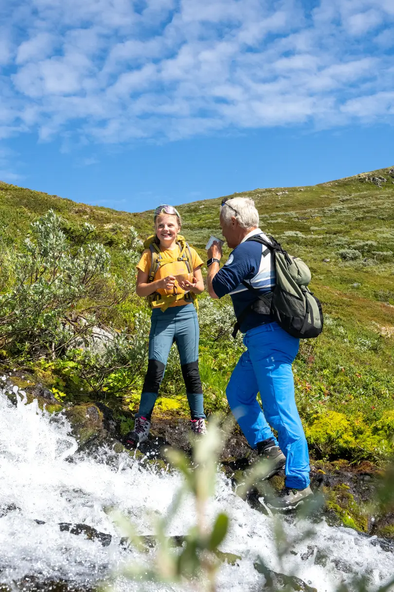 Bestefar og barn tar en drikkepause med fjellvann fra bekken under fjelltur