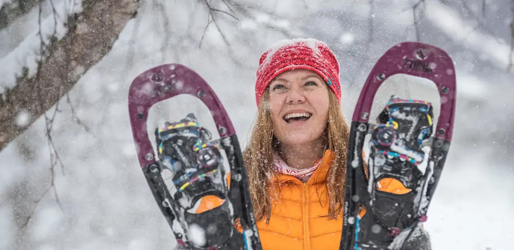 Glad kvinde holder et par snesko op, mens det sner