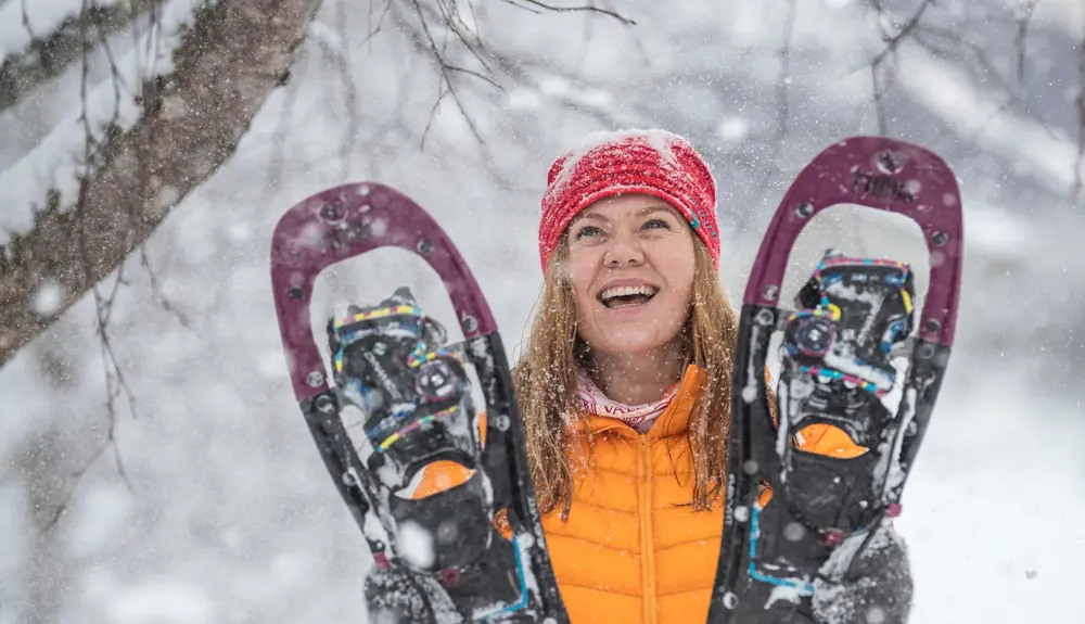 Glad kvinne som holder opp et par med truger mens det snør